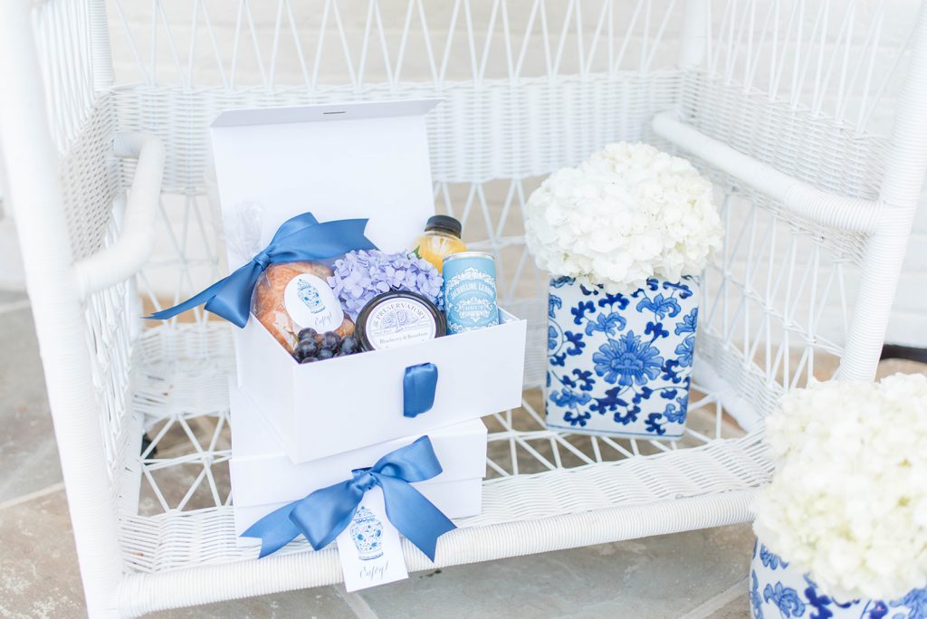 A brunch-themed wedding welcome gift designed by The Welcoming District. These pretty gifts welcomed guests at Catesby Farm Estate in Virginia. Gift goodies included a croissant, grapes, fresh orange juice, champagne, and blueberry preserves. Each was finished with blue satin ribbon and ginger jar gift tags and labels.